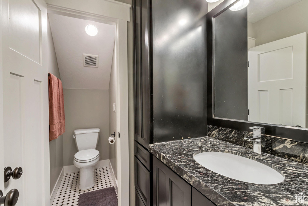 Bathroom featuring vanity, toilet, vaulted ceiling, and tile flooring