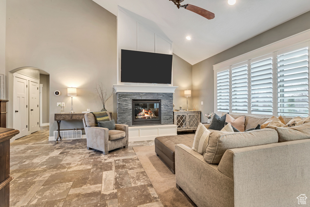 Living room featuring light tile flooring, a fireplace, ceiling fan, and high vaulted ceiling