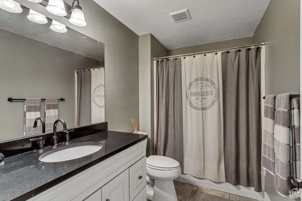 Full bathroom with a textured ceiling, shower / tub combo with curtain, oversized vanity, toilet, and tile flooring