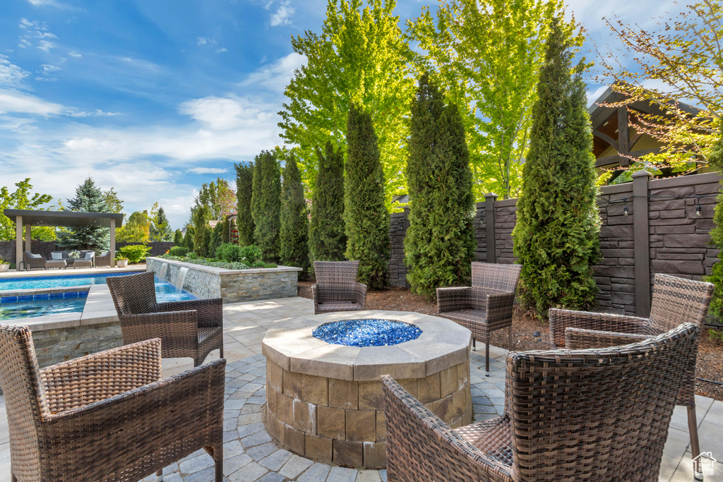View of patio with pool water feature and a fire pit