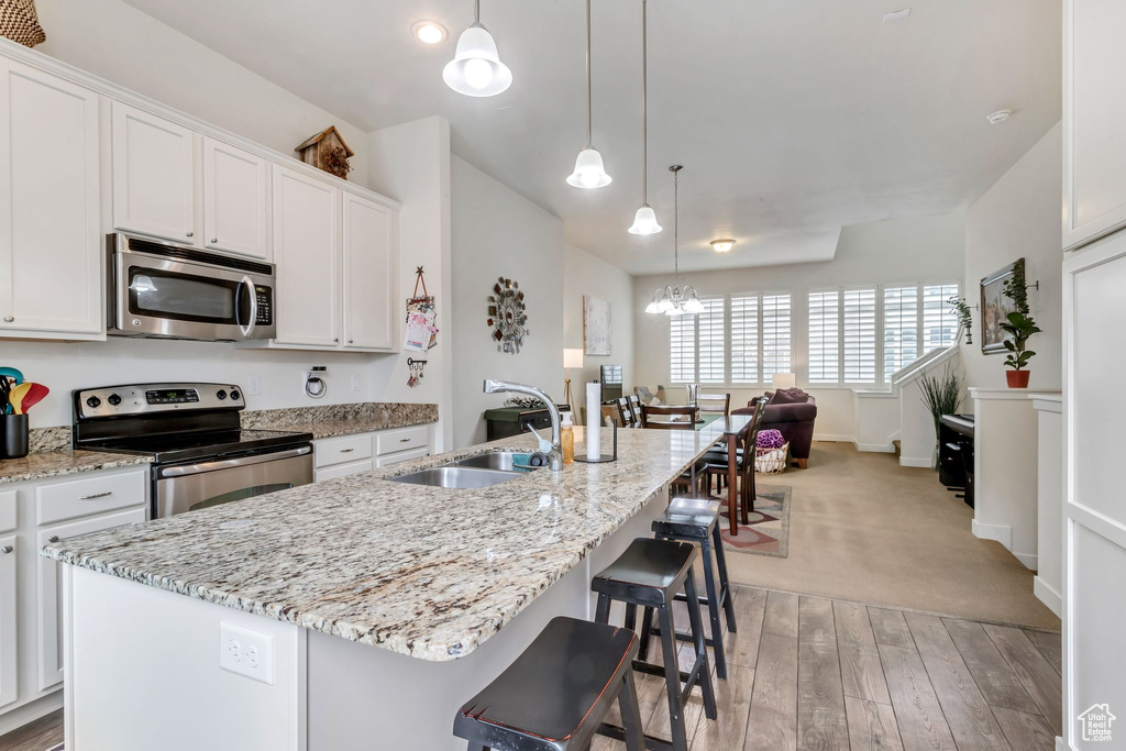 Kitchen featuring an island with sink, appliances with stainless steel finishes, an inviting chandelier, and light carpet