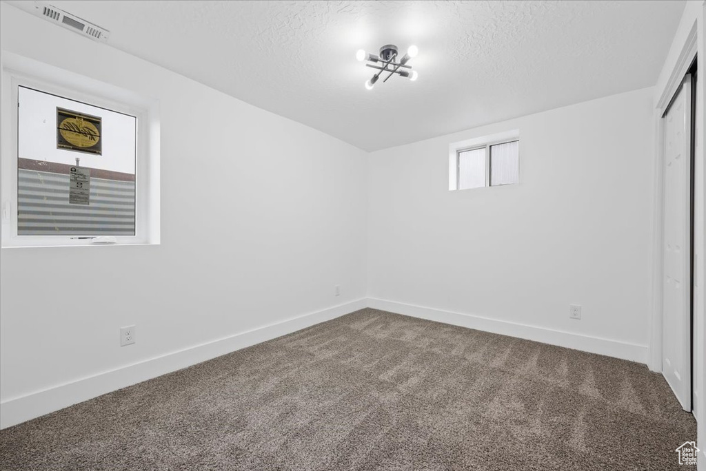 Empty room with an inviting chandelier, a textured ceiling, and carpet flooring