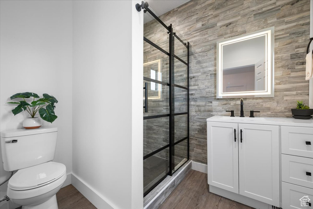 Bathroom featuring hardwood / wood-style floors, vanity, toilet, a shower with door, and wooden walls