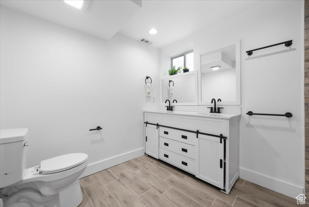 Bathroom featuring toilet, vanity with extensive cabinet space, and wood-type flooring