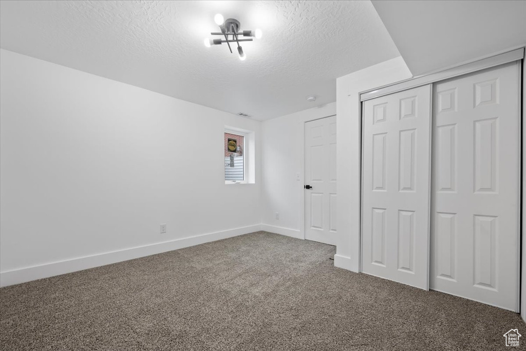 Unfurnished bedroom featuring a closet, dark colored carpet, and a textured ceiling