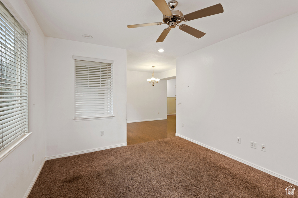 Unfurnished room with dark carpet and ceiling fan with notable chandelier