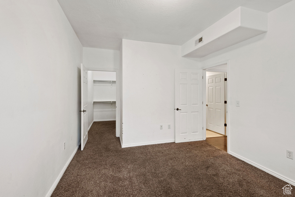 Unfurnished bedroom featuring dark carpet, a walk in closet, and a closet