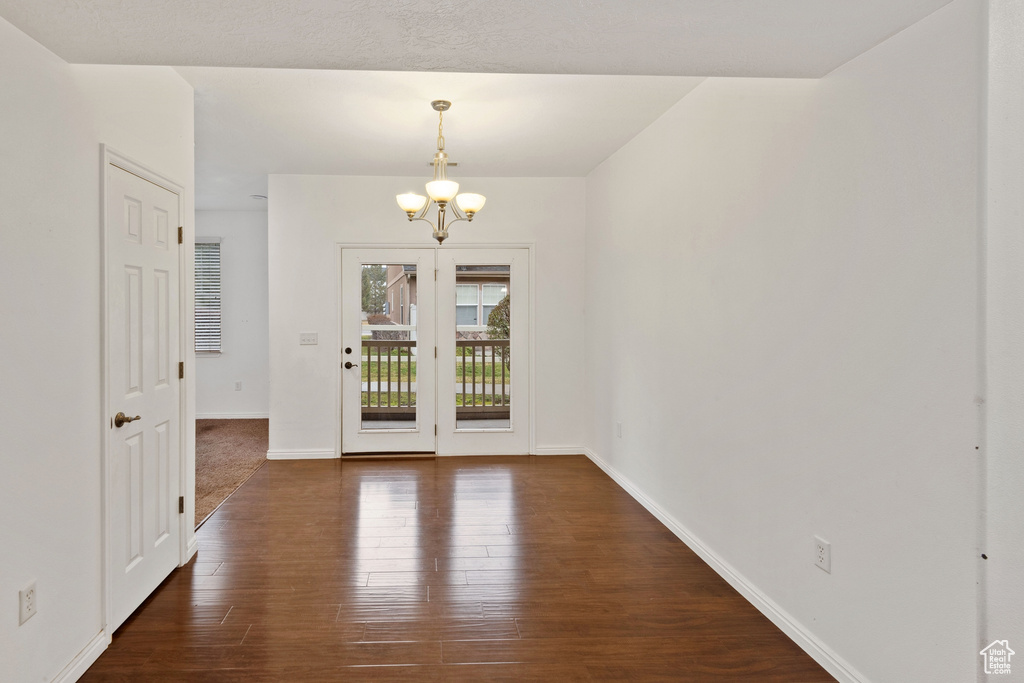 Empty room with dark hardwood / wood-style flooring and a notable chandelier
