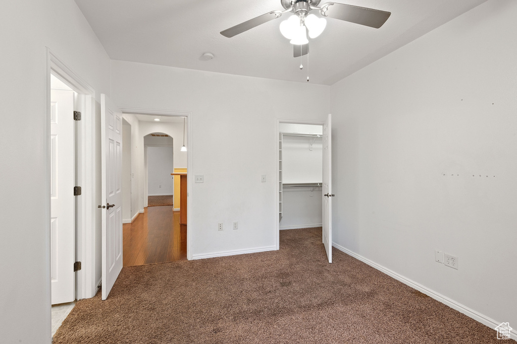 Unfurnished bedroom with a spacious closet, ceiling fan, dark carpet, and a closet