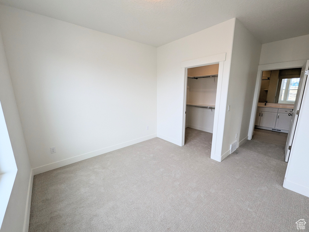 Unfurnished bedroom with a walk in closet, light carpet, and a closet