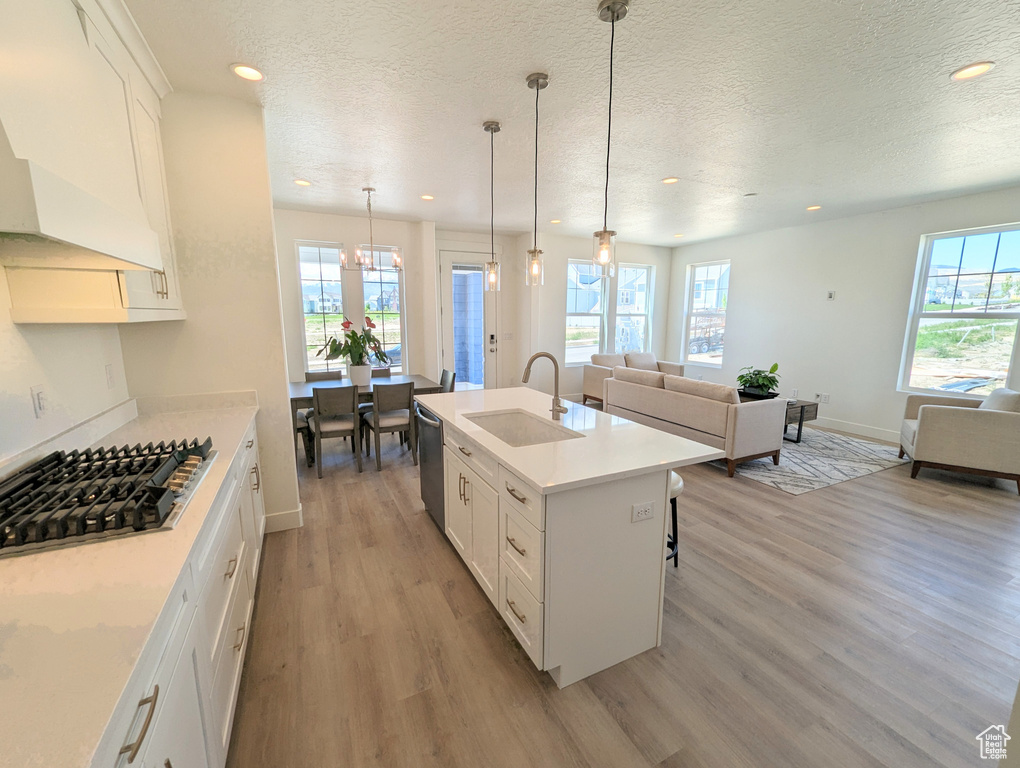 Kitchen featuring a center island with sink, white cabinetry, sink, and light wood-type flooring