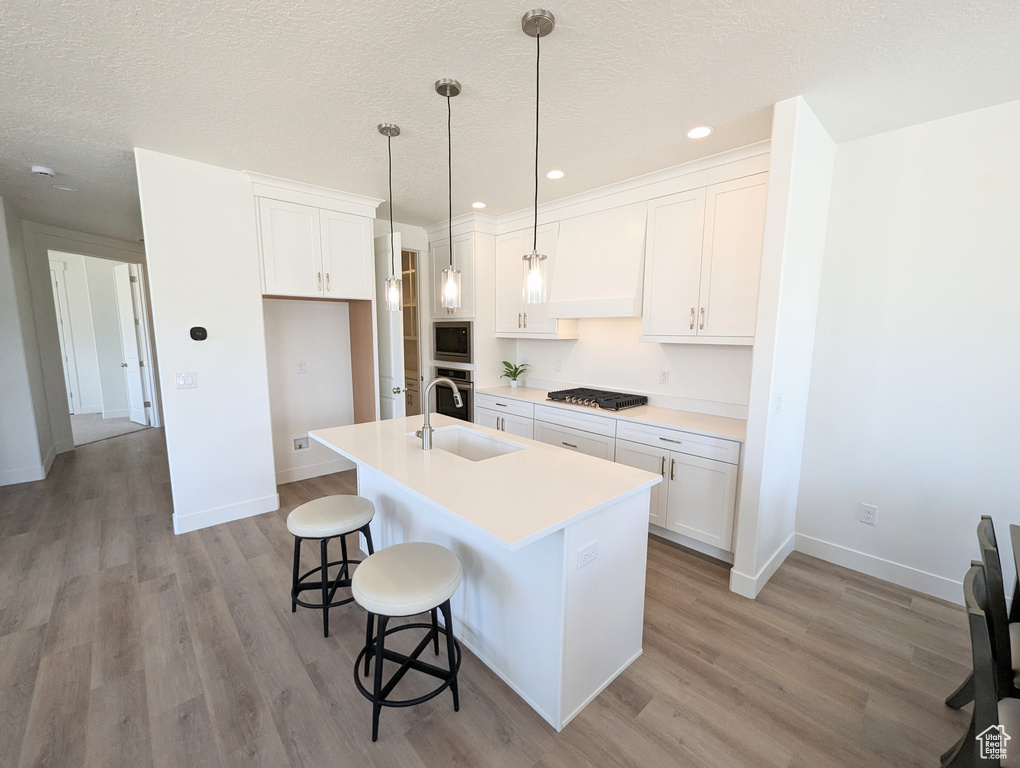 Kitchen featuring white cabinets, hanging light fixtures, sink, and light wood-type flooring