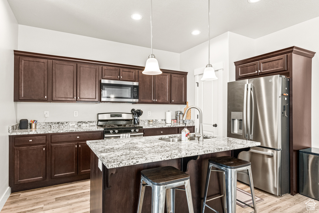 Kitchen featuring appliances with stainless steel finishes, light stone countertops, decorative light fixtures, and light wood-type flooring