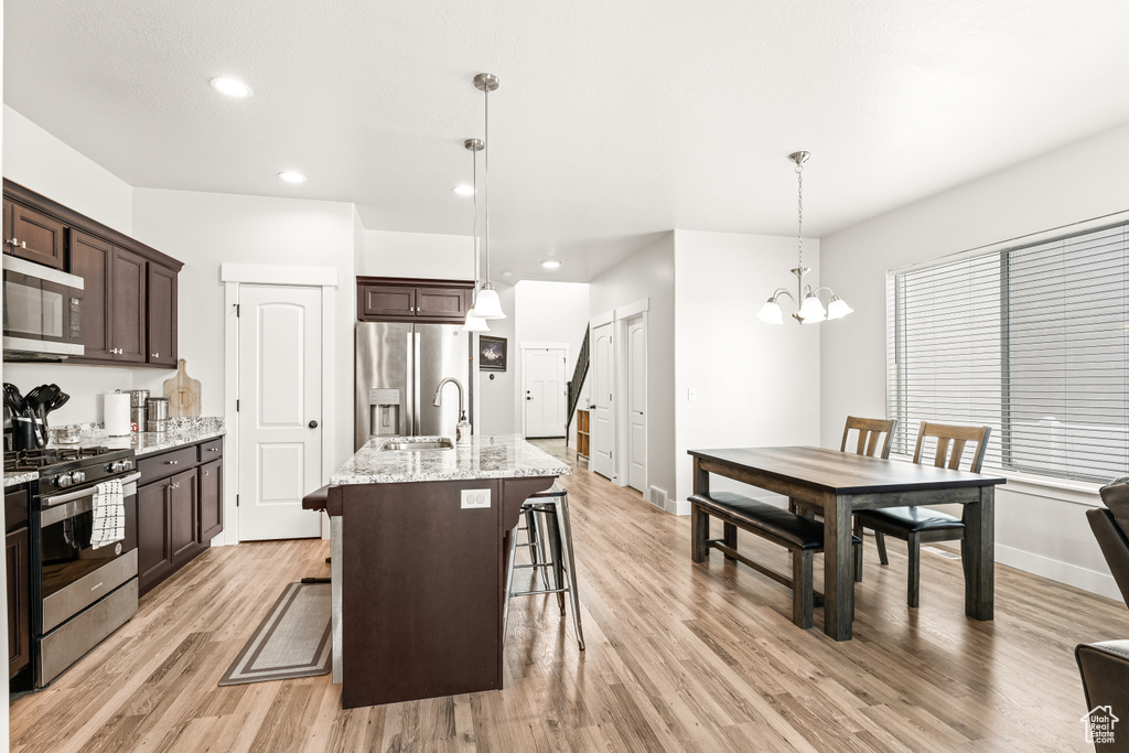 Kitchen featuring light wood-type flooring, a breakfast bar area, hanging light fixtures, an inviting chandelier, and stainless steel appliances