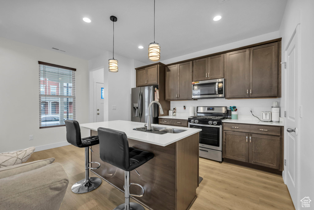 Kitchen with a kitchen bar, appliances with stainless steel finishes, light hardwood / wood-style flooring, sink, and decorative light fixtures