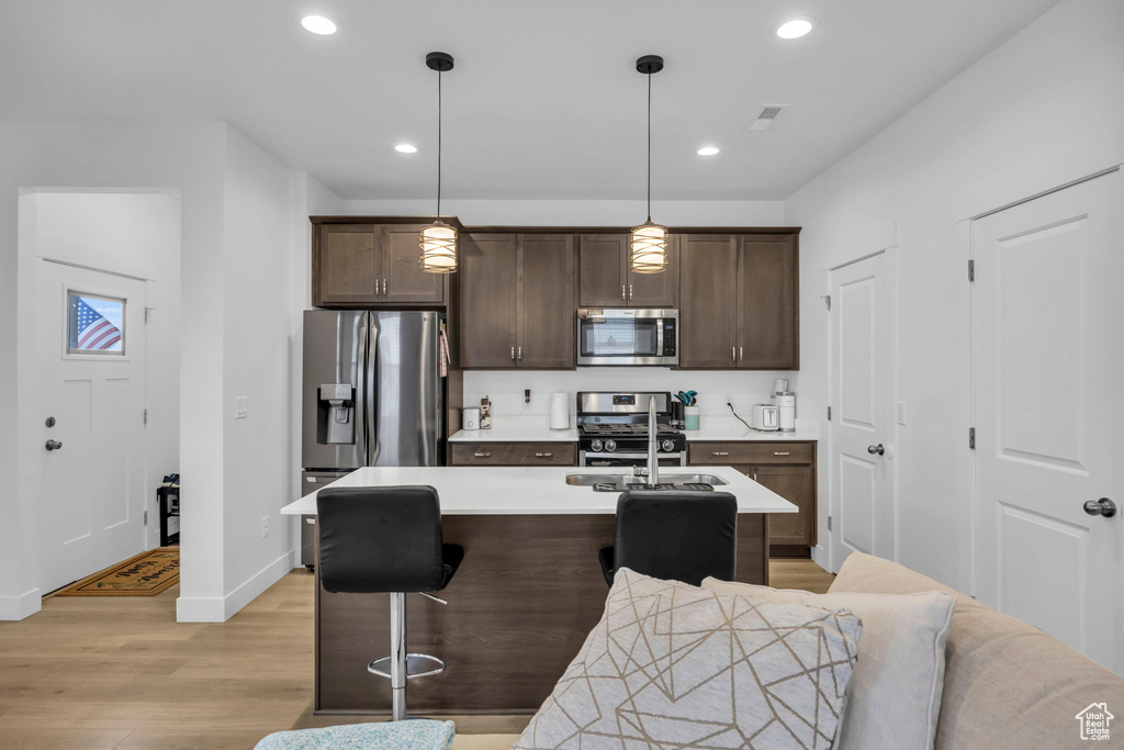 Kitchen featuring light wood-type flooring, pendant lighting, stainless steel appliances, a breakfast bar, and an island with sink