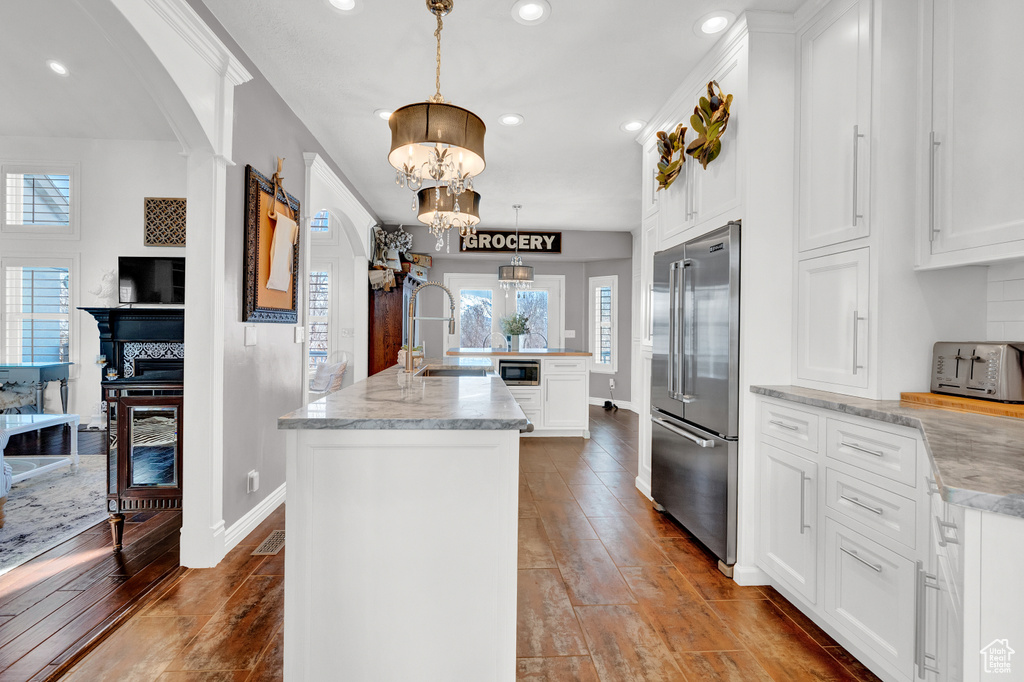 Kitchen with a notable chandelier, stainless steel appliances, white cabinets, hanging light fixtures, and a kitchen island with sink