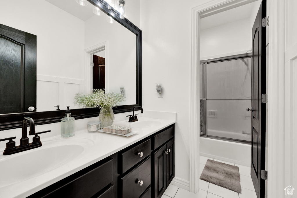 Bathroom with combined bath / shower with glass door, tile floors, oversized vanity, and double sink