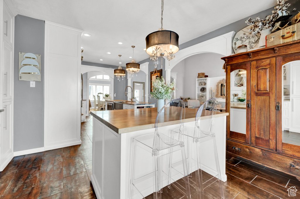 Kitchen with white cabinetry, a chandelier, dark tile flooring, hanging light fixtures, and a kitchen island with sink