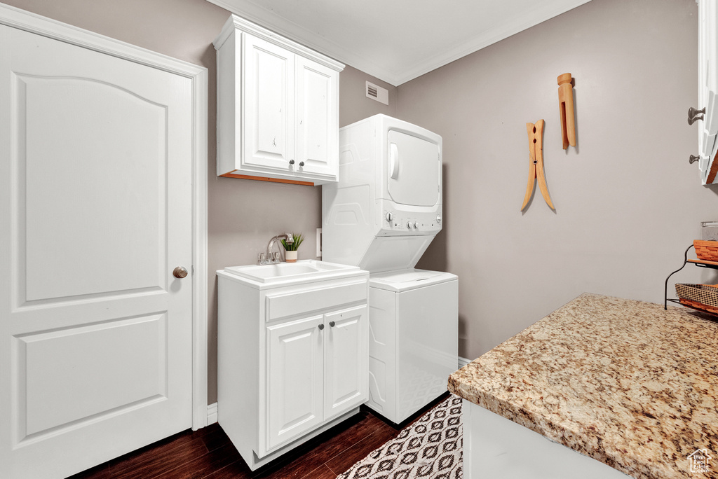Washroom with dark hardwood / wood-style floors, cabinets, stacked washer and clothes dryer, and sink
