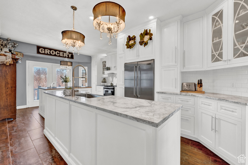 Kitchen featuring pendant lighting, stainless steel appliances, white cabinets, a chandelier, and backsplash