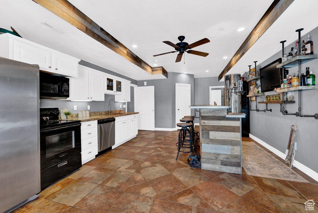 Kitchen with black appliances, a breakfast bar area, ceiling fan, white cabinetry, and dark tile floors