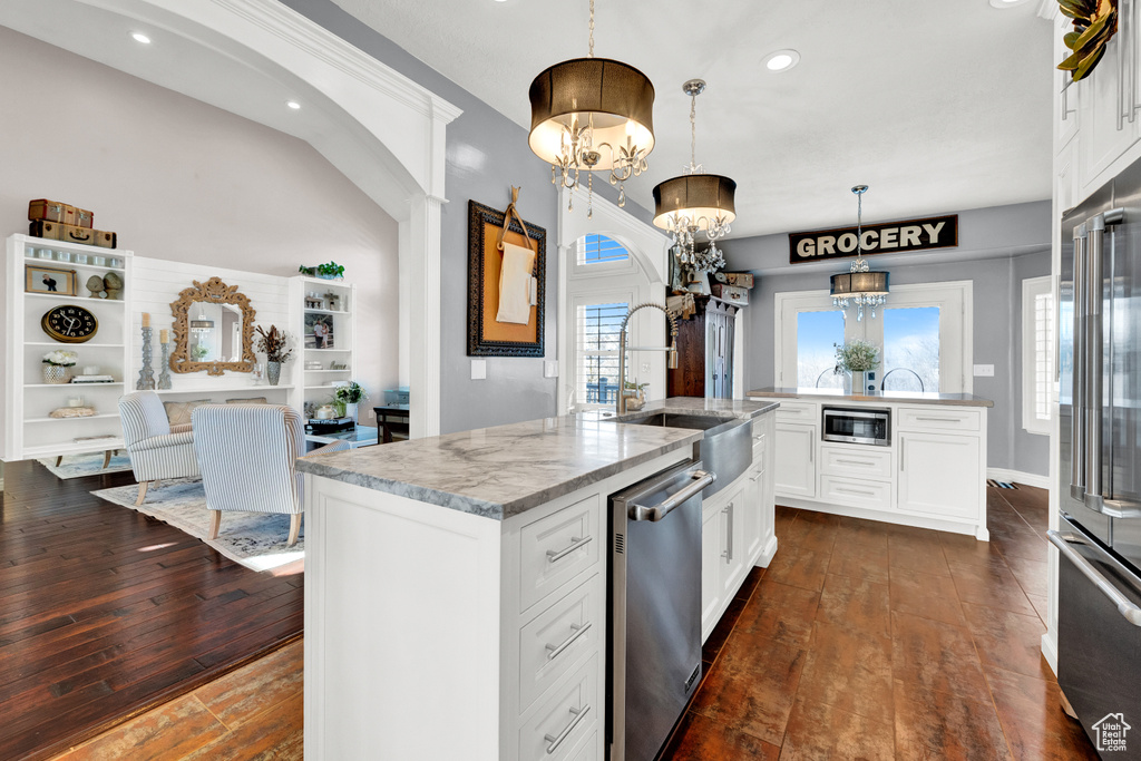Kitchen with hanging light fixtures, dark wood-type flooring, an inviting chandelier, and a center island with sink