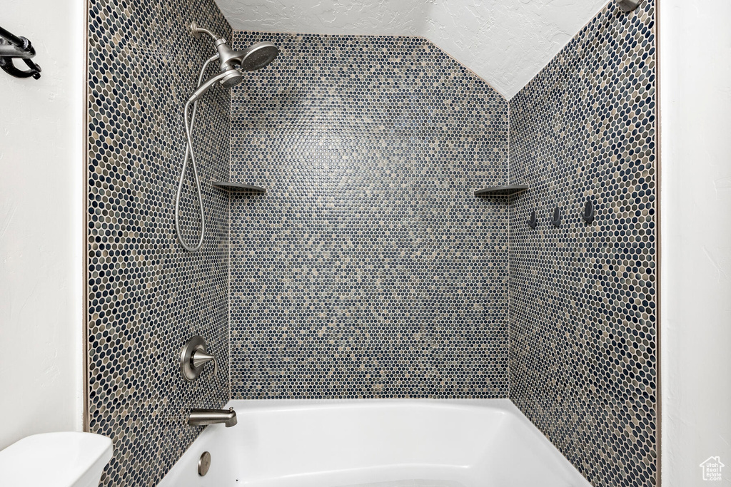 Bathroom featuring toilet, vaulted ceiling, and tiled shower / bath