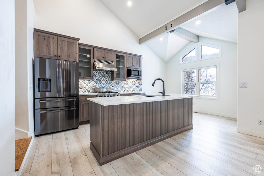 Kitchen featuring an island with sink, beam ceiling, light hardwood / wood-style flooring, appliances with stainless steel finishes, and sink