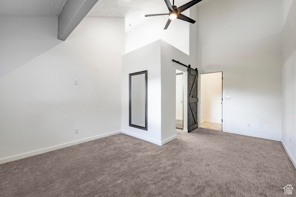 Interior space featuring ceiling fan, a barn door, high vaulted ceiling, light carpet, and a textured ceiling