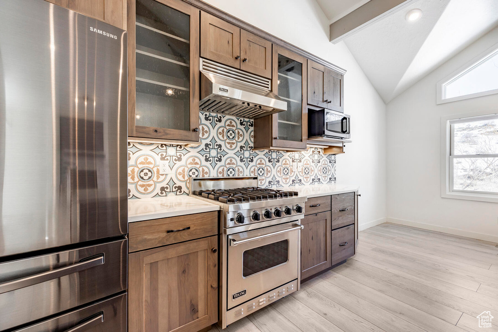 Kitchen with appliances with stainless steel finishes, light hardwood / wood-style flooring, backsplash, wall chimney range hood, and vaulted ceiling with beams