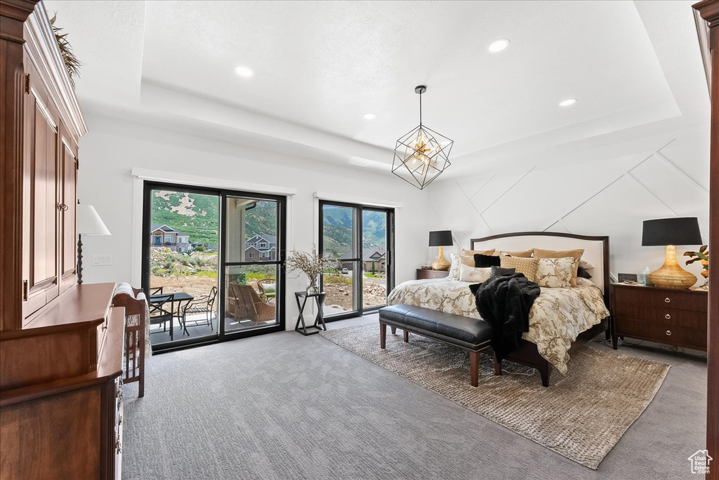 Carpeted bedroom with access to outside, a notable chandelier, and a tray ceiling