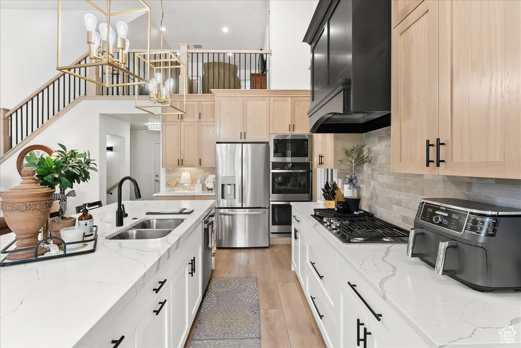 Kitchen featuring stainless steel appliances, custom range hood, tasteful backsplash, light hardwood / wood-style flooring, and sink