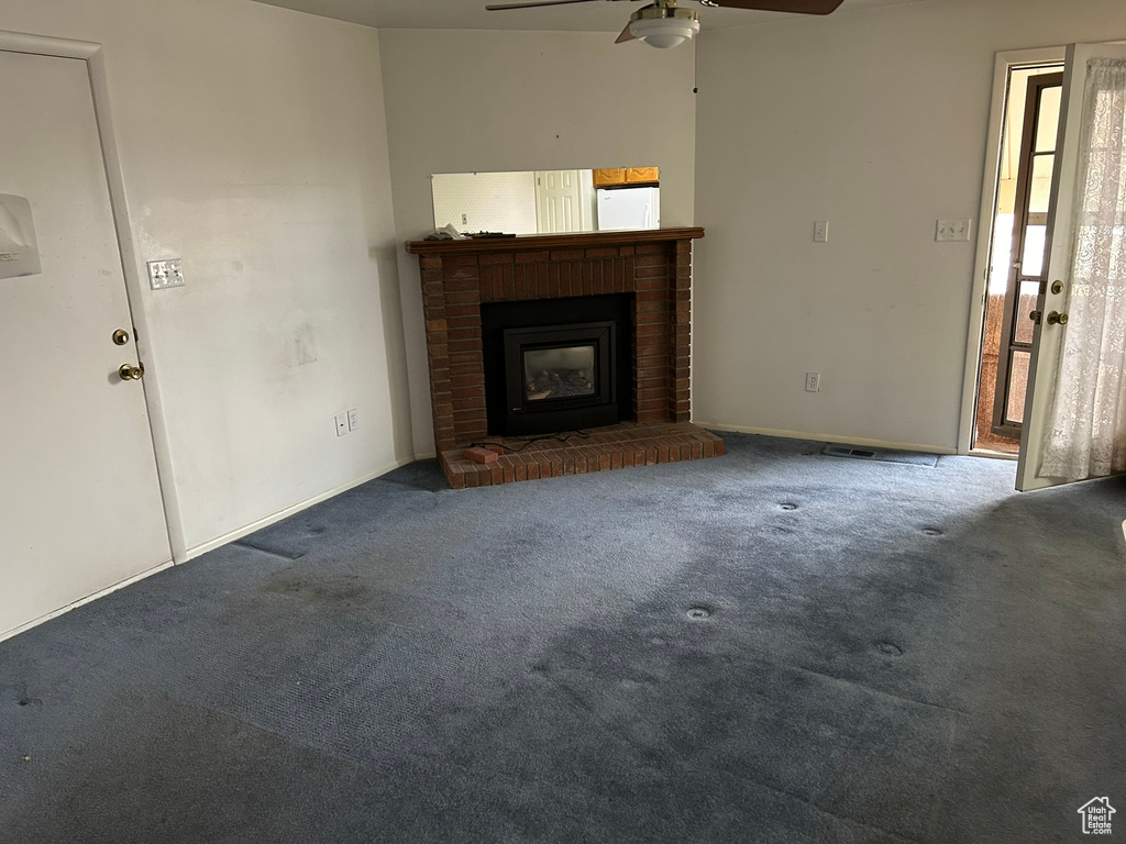 Unfurnished living room with dark colored carpet, a brick fireplace, and ceiling fan
