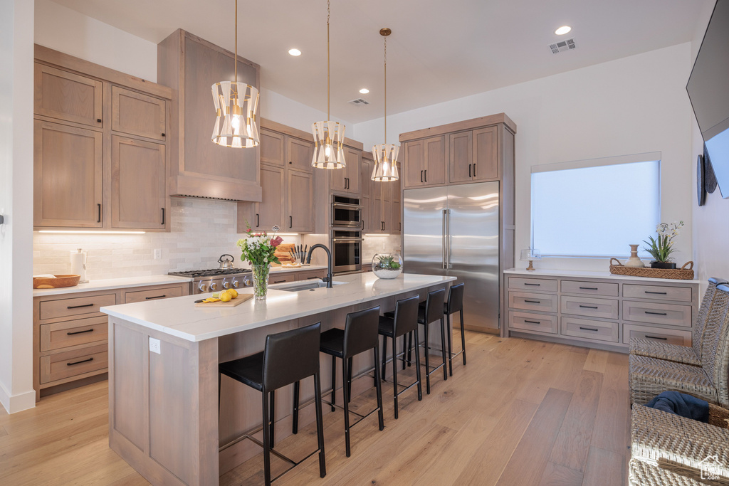 Kitchen featuring light hardwood / wood-style flooring, a breakfast bar, a kitchen island with sink, and tasteful backsplash