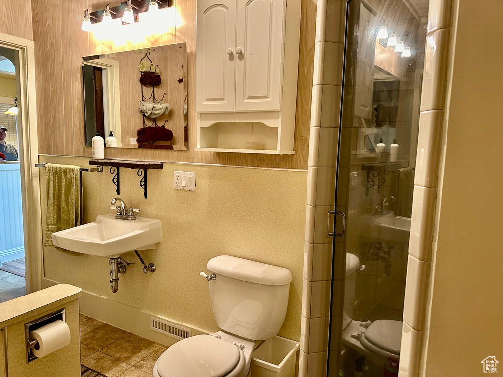 Bathroom featuring sink, a shower with door, tile floors, and toilet