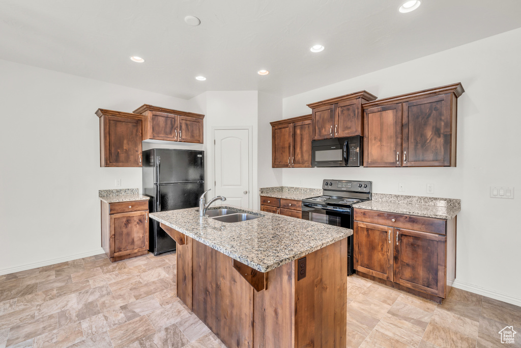 Kitchen featuring light stone countertops, black appliances, an island with sink, sink, and light tile floors