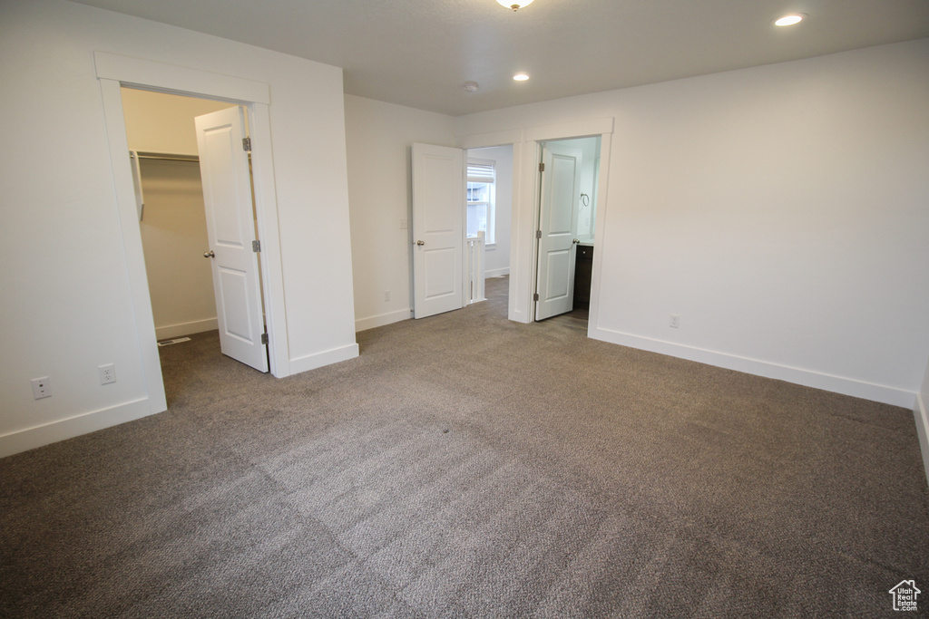 Unfurnished bedroom featuring ensuite bath, a walk in closet, dark colored carpet, and a closet