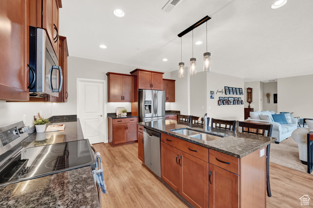 Kitchen featuring light hardwood / wood-style floors, a center island with sink, sink, decorative light fixtures, and appliances with stainless steel finishes