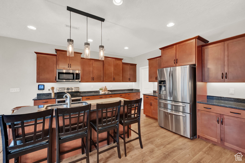Kitchen with pendant lighting, stainless steel appliances, a center island with sink, light hardwood / wood-style flooring, and a kitchen breakfast bar