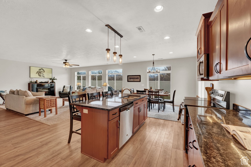 Kitchen with pendant lighting, ceiling fan with notable chandelier, stainless steel appliances, light hardwood / wood-style flooring, and an island with sink