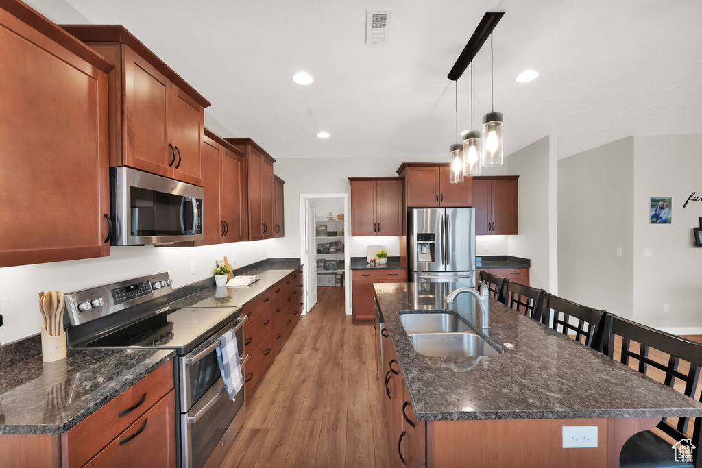 Kitchen featuring light hardwood / wood-style floors, a center island with sink, a kitchen bar, pendant lighting, and appliances with stainless steel finishes
