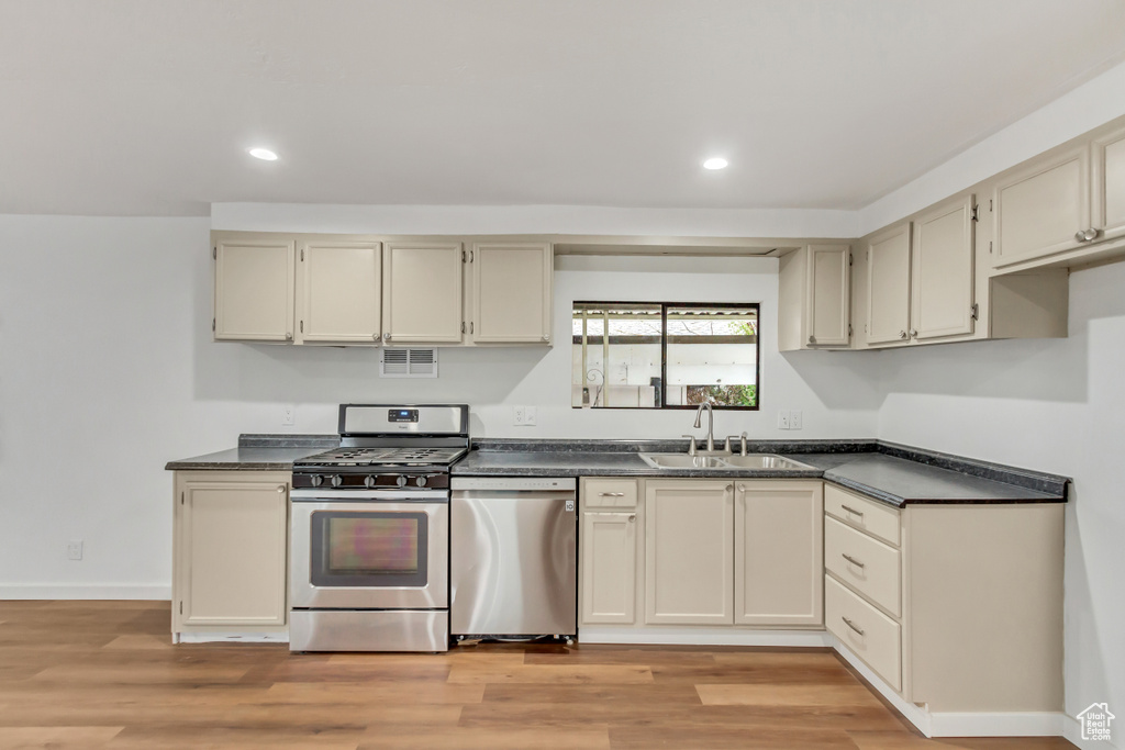 Kitchen with appliances with stainless steel finishes, light hardwood / wood-style floors, cream cabinetry, and sink
