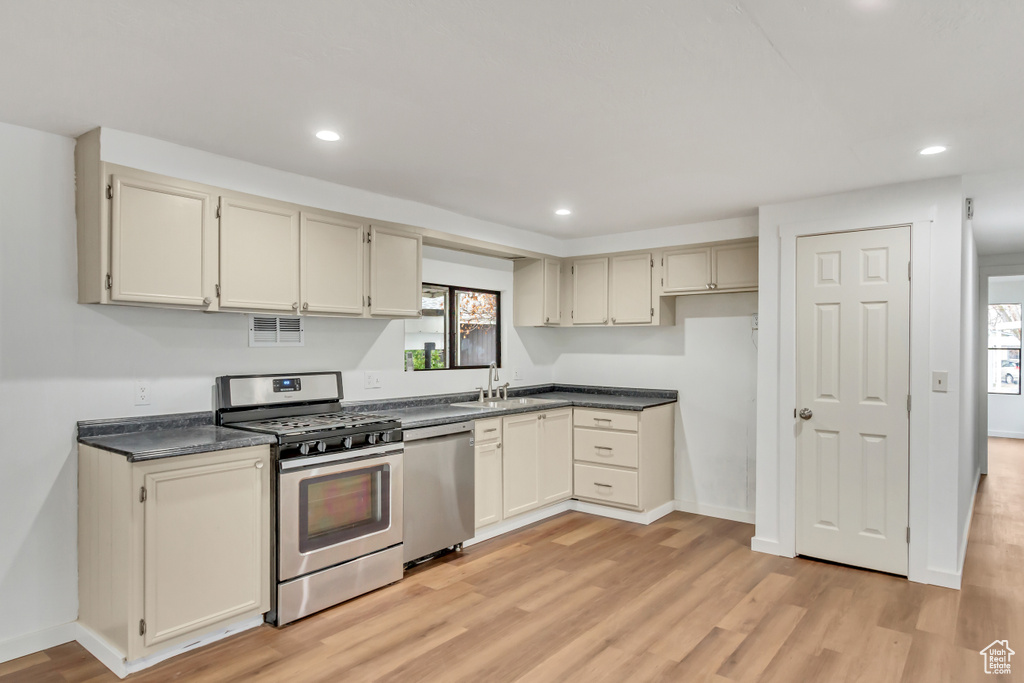 Kitchen featuring appliances with stainless steel finishes, light hardwood / wood-style flooring, cream cabinets, and sink