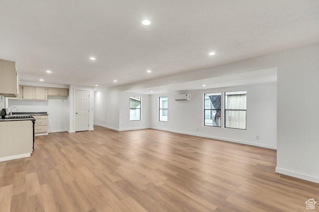 Unfurnished living room featuring light hardwood / wood-style flooring and a wall unit AC
