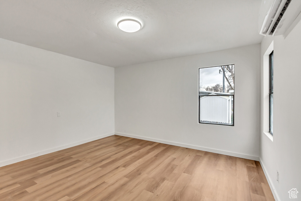 Empty room featuring light hardwood / wood-style floors, a wall unit AC, and a healthy amount of sunlight