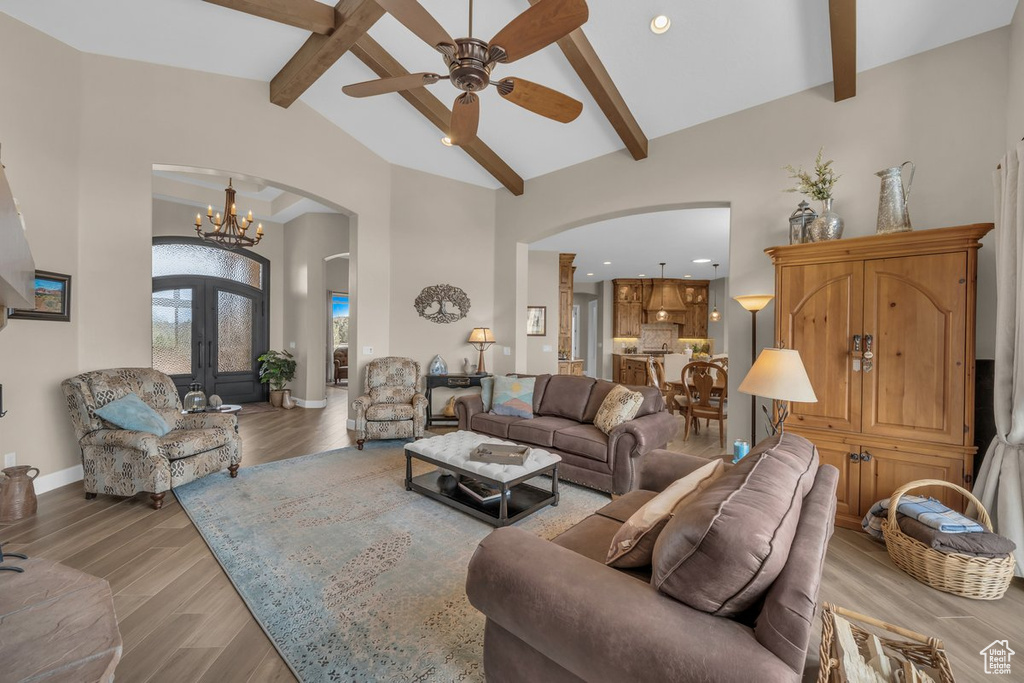 Living room with light hardwood / wood-style floors, ceiling fan with notable chandelier, vaulted ceiling with beams, and french doors