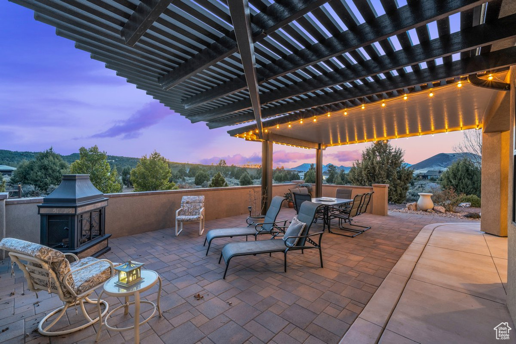 Patio terrace at dusk with a pergola and exterior fireplace
