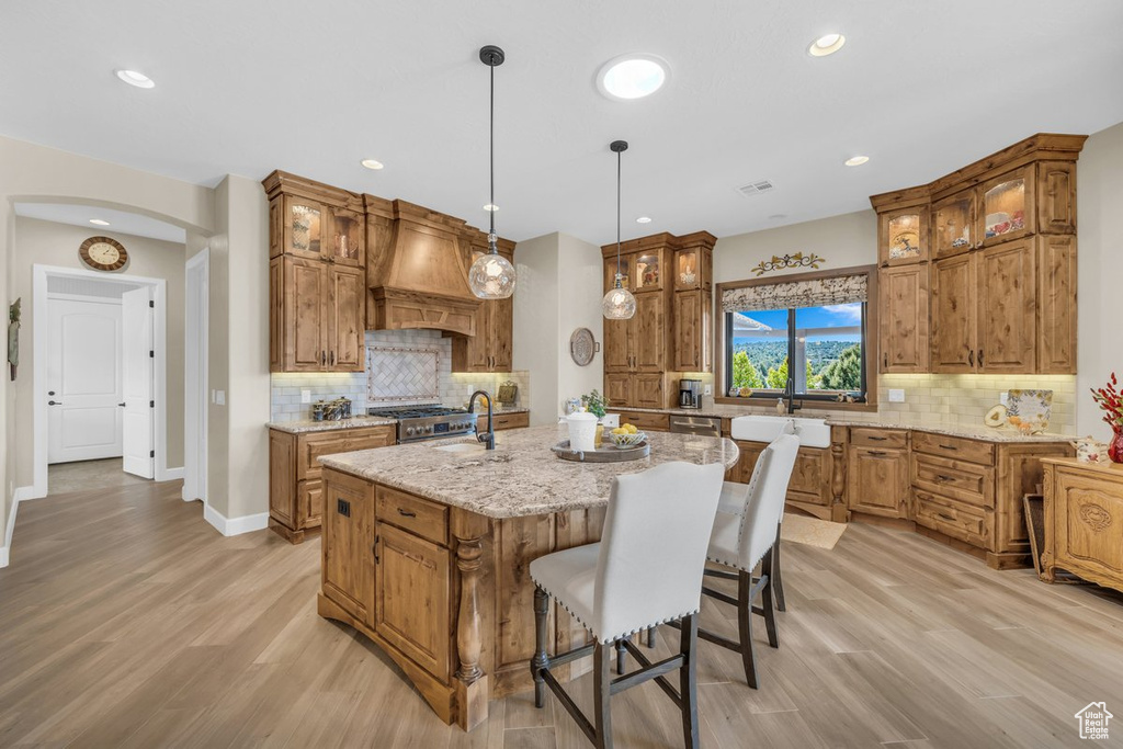 Kitchen with a center island with sink, custom range hood, light wood-type flooring, and backsplash