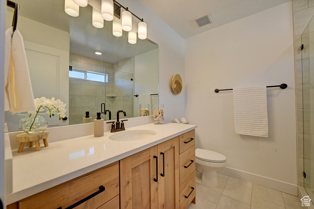 Bathroom with toilet, a shower with shower door, vanity with extensive cabinet space, and tile flooring